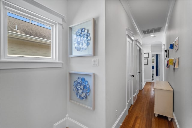 corridor featuring dark wood-style floors, baseboards, visible vents, and ornamental molding