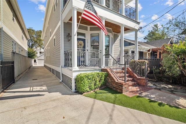 shotgun-style home with a balcony, covered porch, and fence