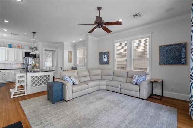 living area with baseboards, visible vents, wood finished floors, and ornamental molding