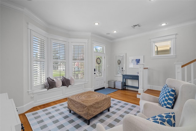 living area with light wood-type flooring, visible vents, and crown molding