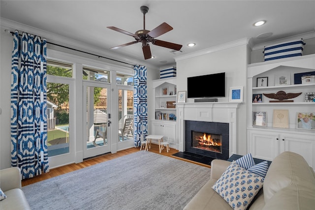 living area with a tile fireplace, recessed lighting, light wood-style floors, built in features, and crown molding