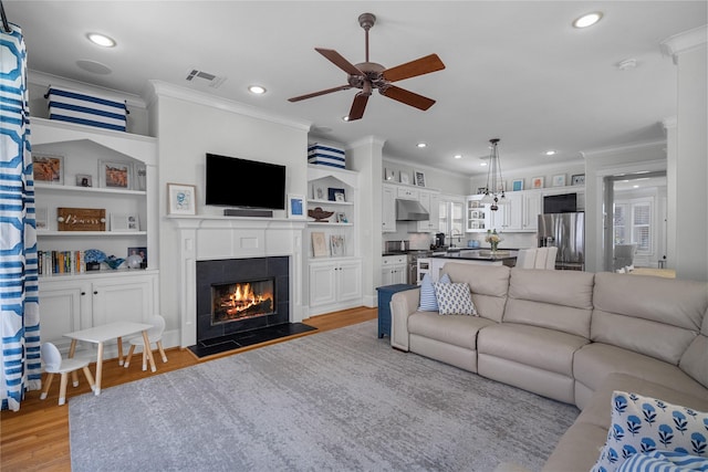 living room featuring crown molding, light wood-type flooring, a tile fireplace, and recessed lighting