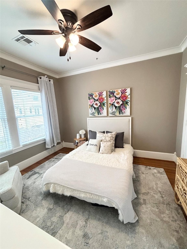 bedroom featuring baseboards, wood finished floors, visible vents, and crown molding