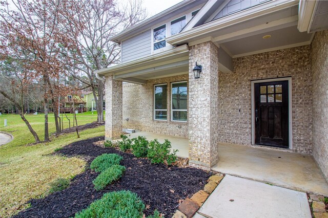 property entrance featuring board and batten siding, covered porch, brick siding, and a lawn