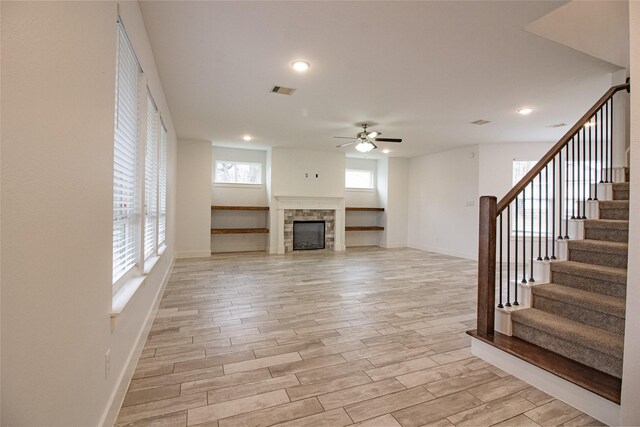 unfurnished living room featuring a fireplace, a ceiling fan, baseboards, stairway, and light wood finished floors