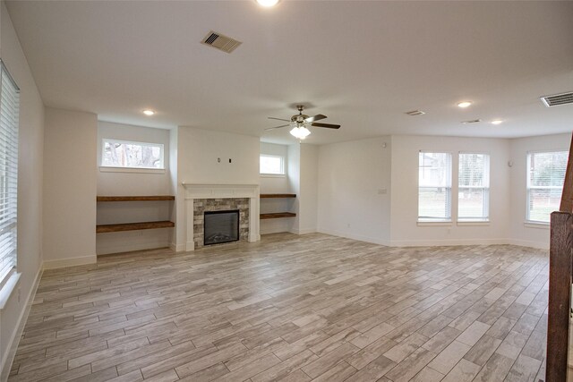 unfurnished living room with ceiling fan, a fireplace, visible vents, and light wood-style floors