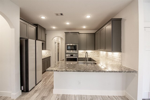 kitchen featuring arched walkways, a sink, built in microwave, oven, and a peninsula