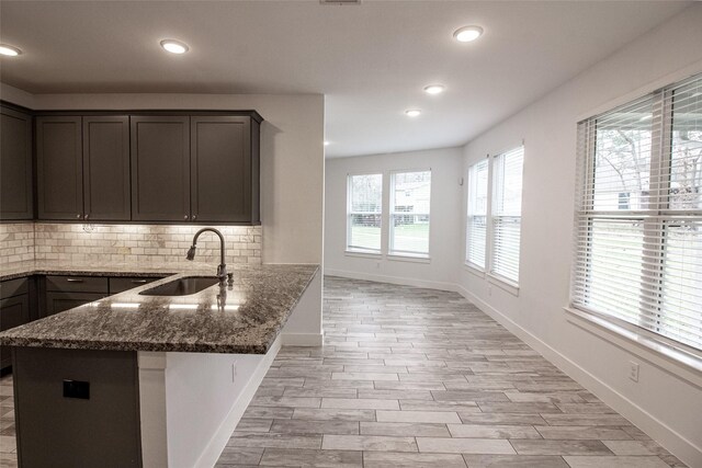 kitchen featuring decorative backsplash, a sink, dark brown cabinets, dark stone counters, and a peninsula