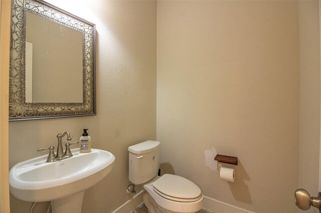 half bathroom with a sink, toilet, and baseboards