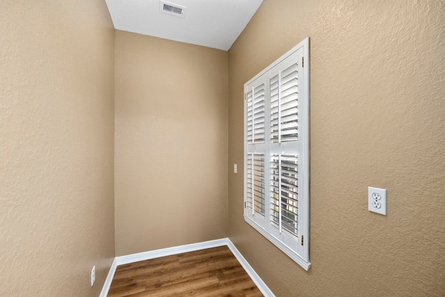 interior space featuring a textured wall, wood finished floors, visible vents, and baseboards