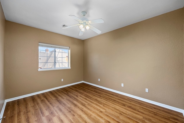 empty room with ceiling fan, wood finished floors, visible vents, and baseboards