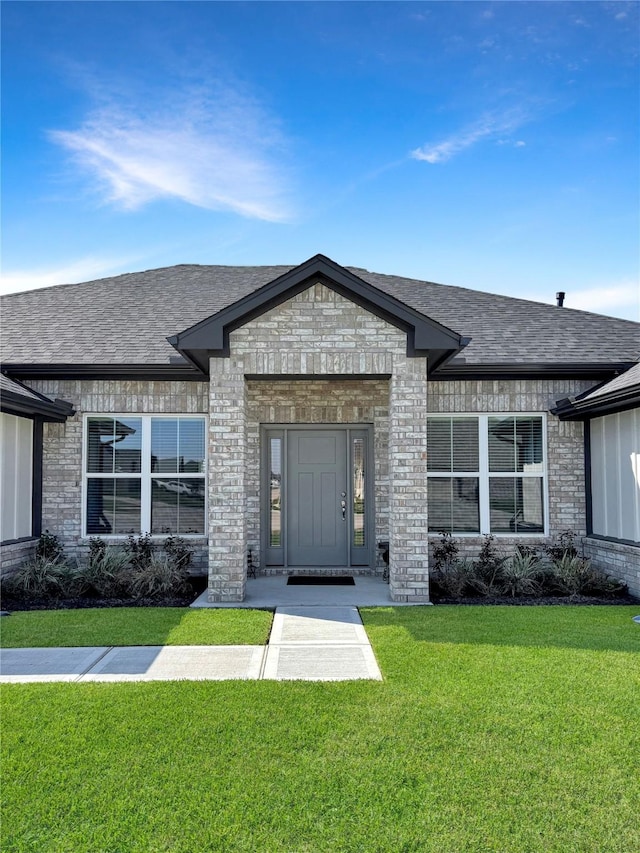 doorway to property featuring a yard, brick siding, and roof with shingles