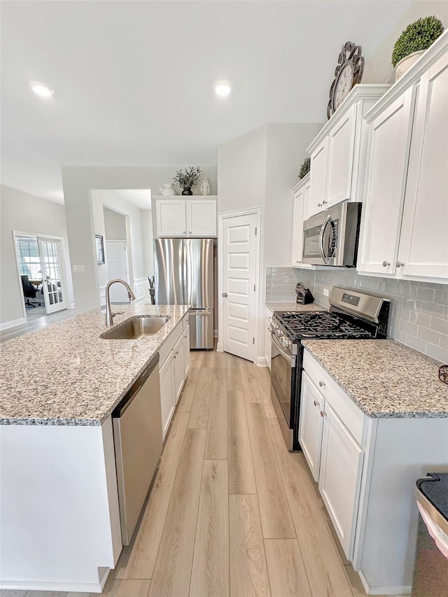 kitchen featuring appliances with stainless steel finishes, a sink, light wood-type flooring, white cabinetry, and backsplash