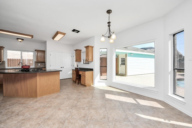 kitchen with dark countertops, hanging light fixtures, an inviting chandelier, light tile patterned flooring, and a sink