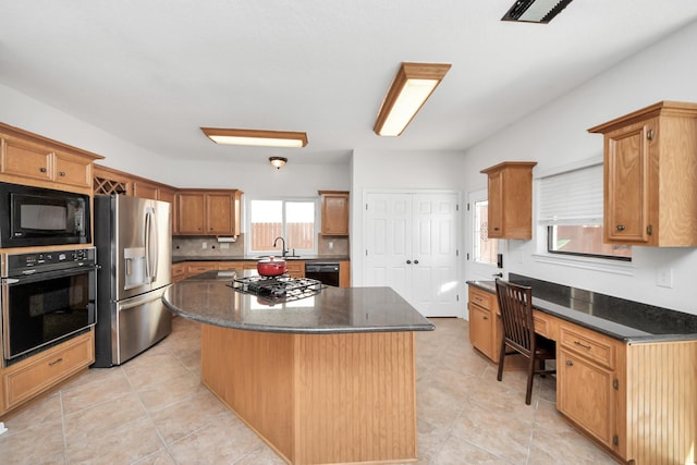 kitchen featuring built in study area, dark stone countertops, a center island, black appliances, and a sink