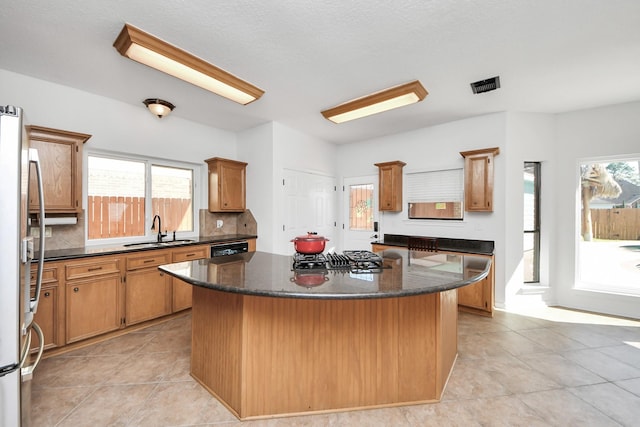 kitchen with decorative backsplash, freestanding refrigerator, a kitchen island, a sink, and gas cooktop