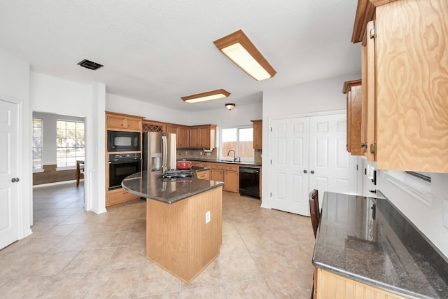 kitchen with a kitchen island, a sink, visible vents, black appliances, and dark stone countertops