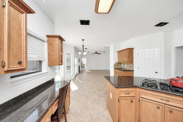 kitchen featuring decorative backsplash, open floor plan, ceiling fan, gas cooktop, and dark stone counters