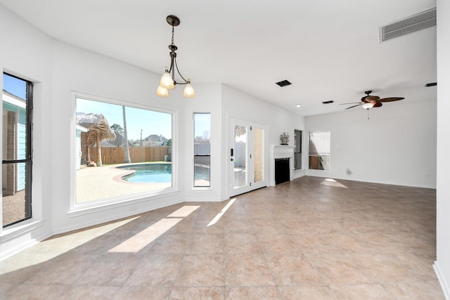 unfurnished living room with ceiling fan with notable chandelier, a fireplace, visible vents, and light tile patterned flooring