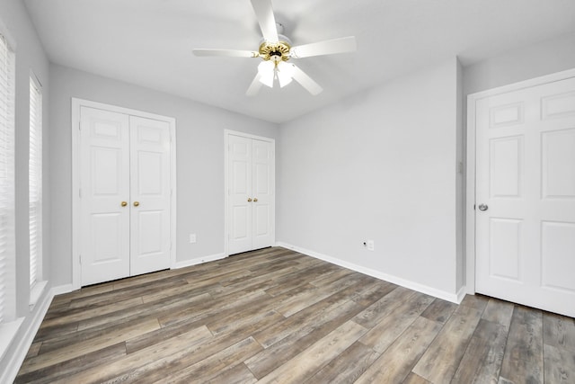 unfurnished bedroom with a ceiling fan, wood finished floors, baseboards, and two closets