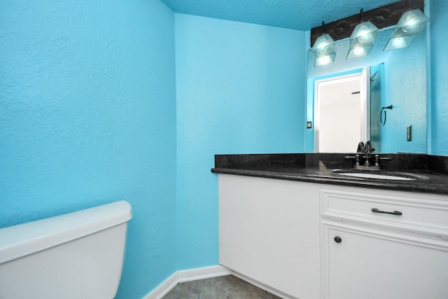 bathroom featuring toilet, a textured wall, baseboards, and vanity