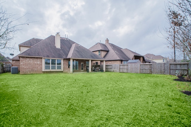 back of property with a lawn, a fenced backyard, a chimney, central air condition unit, and brick siding