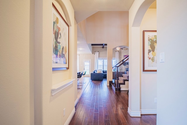 corridor with lofted ceiling, dark wood-style flooring, arched walkways, and baseboards