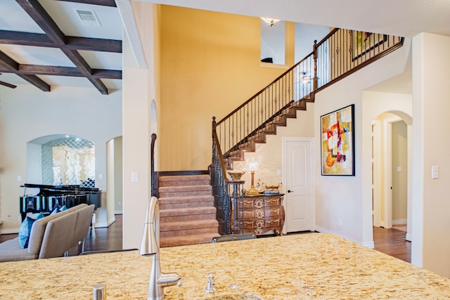 staircase featuring arched walkways, coffered ceiling, wood finished floors, a towering ceiling, and visible vents