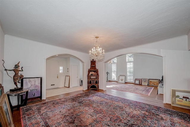 foyer with light wood-style floors, arched walkways, a chandelier, and a textured ceiling