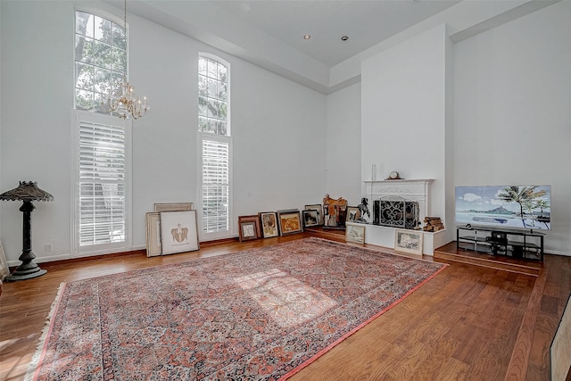 living area with a fireplace with raised hearth, wood finished floors, a towering ceiling, and a notable chandelier