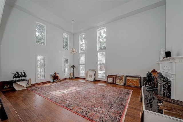 living area featuring a chandelier, a fireplace, wood finished floors, a towering ceiling, and a wealth of natural light