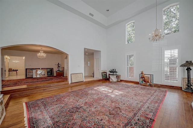 unfurnished living room with a chandelier, arched walkways, visible vents, and wood finished floors