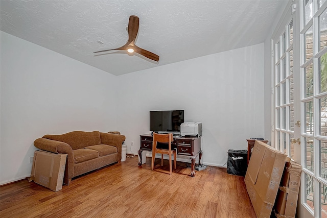 office with a textured ceiling, baseboards, light wood-style flooring, and a ceiling fan