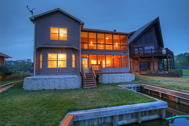 back of house at dusk featuring a sunroom, a lawn, stairway, and a balcony