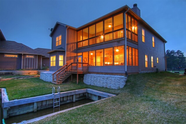 back of property at dusk featuring a balcony, a sunroom, stairs, a yard, and a chimney