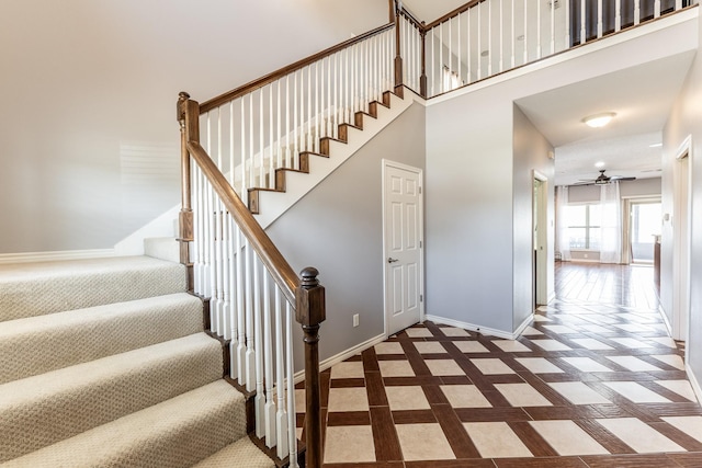 staircase featuring a ceiling fan, a towering ceiling, and baseboards