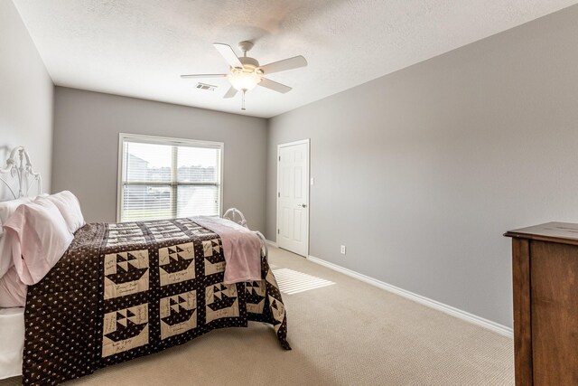 bedroom featuring ceiling fan, a textured ceiling, light colored carpet, visible vents, and baseboards