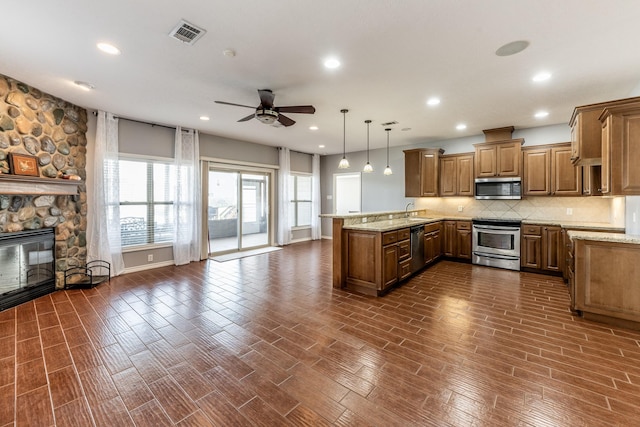 kitchen with a fireplace, stainless steel appliances, hanging light fixtures, brown cabinetry, and a peninsula