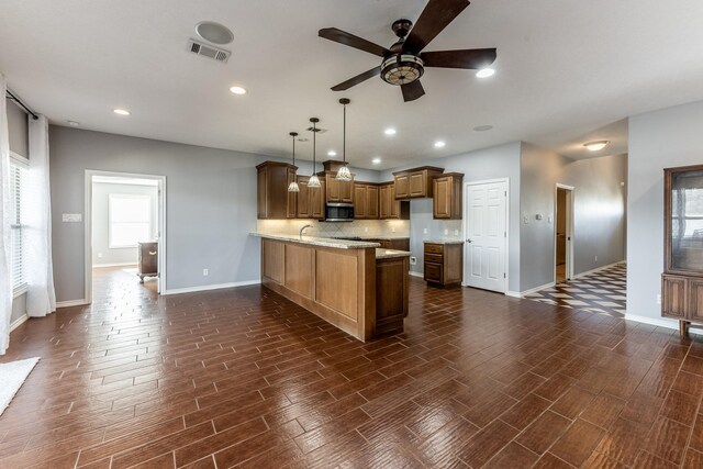 kitchen with visible vents, stainless steel microwave, brown cabinets, a peninsula, and hanging light fixtures