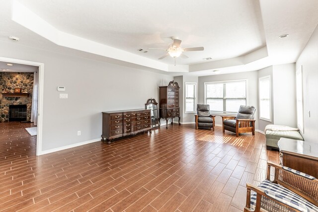 sitting room featuring a stone fireplace, a tray ceiling, dark wood-style flooring, and baseboards