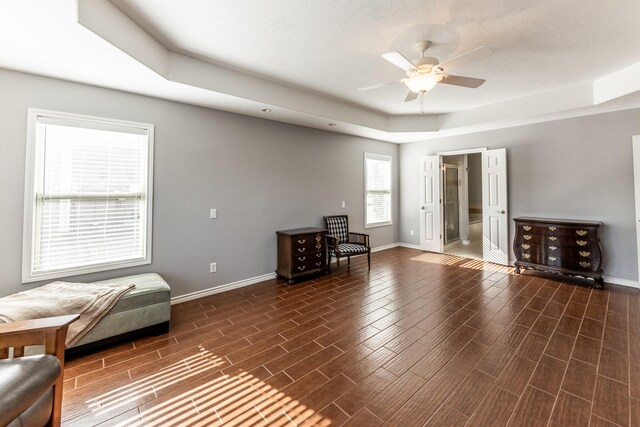 interior space with baseboards, a raised ceiling, a ceiling fan, and wood tiled floor