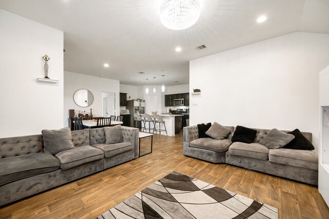 living room featuring a notable chandelier, recessed lighting, visible vents, vaulted ceiling, and light wood-type flooring