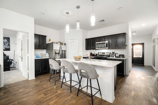 kitchen featuring visible vents, an island with sink, appliances with stainless steel finishes, light countertops, and pendant lighting