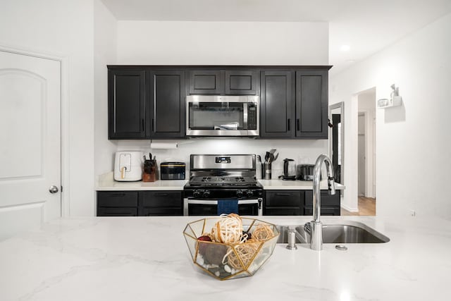 kitchen featuring appliances with stainless steel finishes, a sink, and light stone countertops