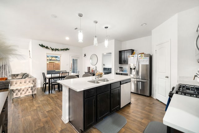 kitchen featuring a kitchen island with sink, stainless steel appliances, dark wood-type flooring, hanging light fixtures, and light countertops