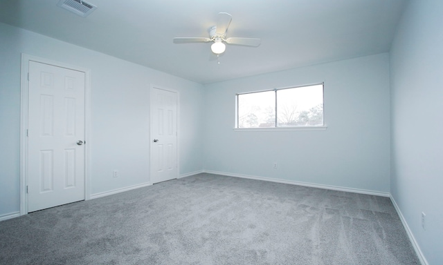 carpeted spare room featuring a ceiling fan, visible vents, and baseboards