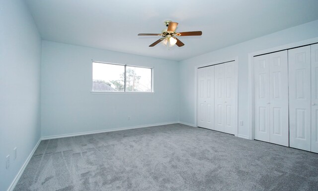 unfurnished bedroom featuring carpet floors, a ceiling fan, baseboards, and two closets