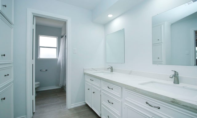 full bath with toilet, double vanity, a sink, and wood finished floors