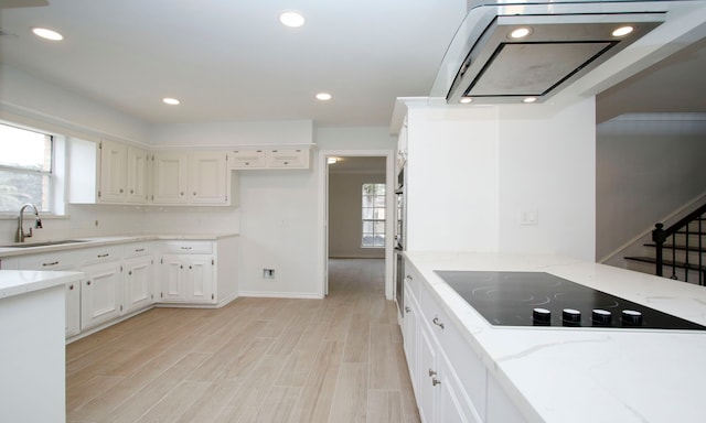 kitchen with light stone countertops, white cabinetry, black electric cooktop, and a sink