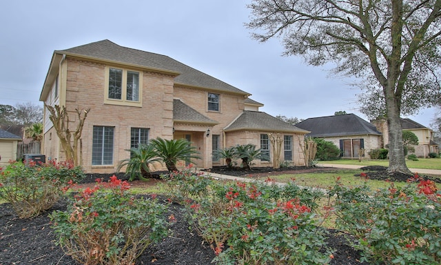 traditional home featuring brick siding, a front lawn, and roof with shingles